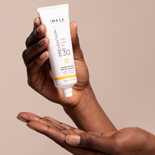 Hand holding a tube of Image Skincare Prevention+ Clear Tinted Gel SPF 30 against a beige background