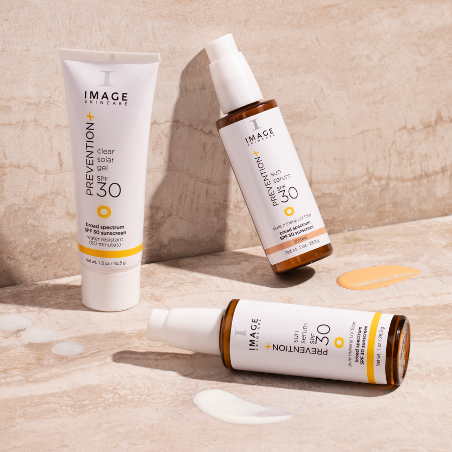 Three bottles of IMAGE Skincare sun protection products on a wooden surface.