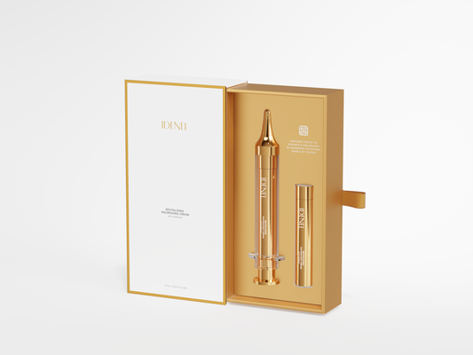 A luxury skincare set by IDENEL, featuring a gold and white outer box with a sliding pull tab, opened to reveal a gold inner tray holding a gold-toned ampoule and a small gold tube, set against a clean white background.